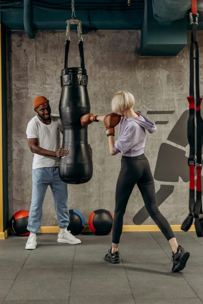 A woman practices boxing with a trainer in a modern gym setting.